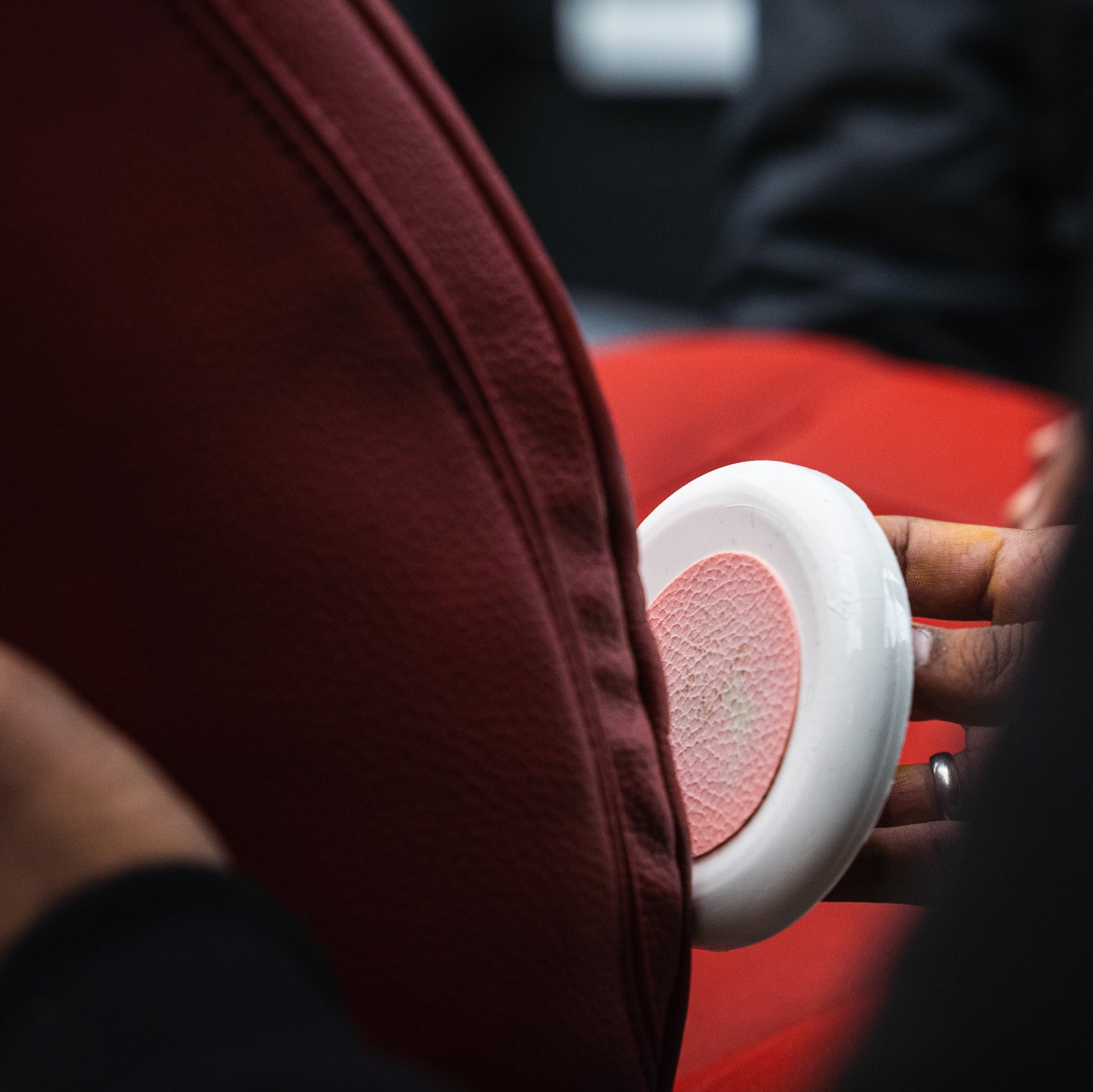 Close-up of a hand holding a white object with a red heart design against a blurred background.