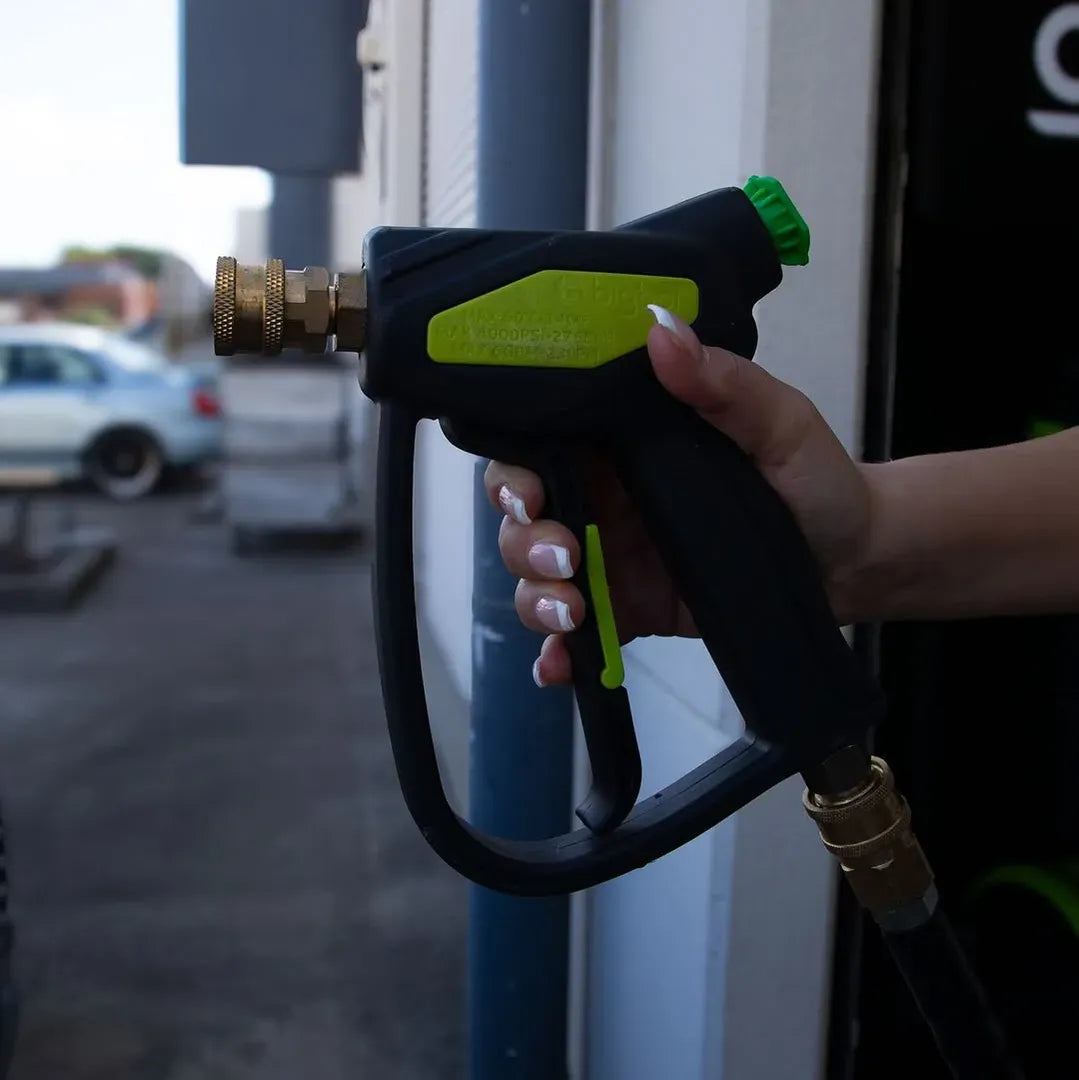 Hand holding a black and green garden hose nozzle in front of a vehicle.