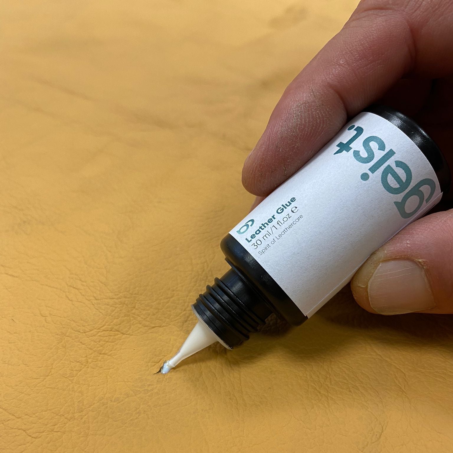 Hand holding a bottle of 'geist' leather glue on a yellow surface