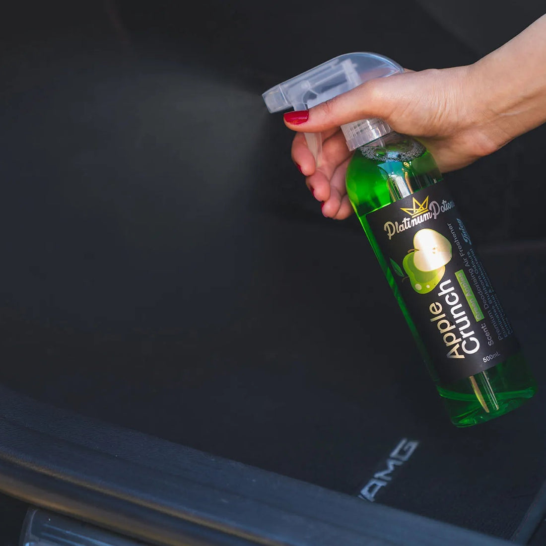 Person holding a bottle of 'Apple Crunch' car freshener over a car's open trunk.