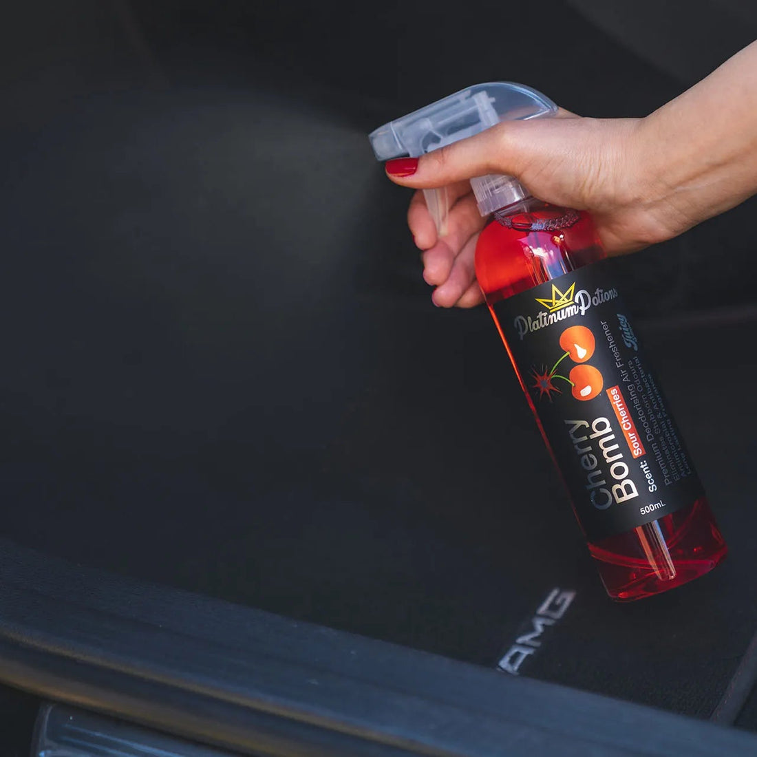 Person using a spray bottle labeled 'Buddy Bomb' on a car's black interior.