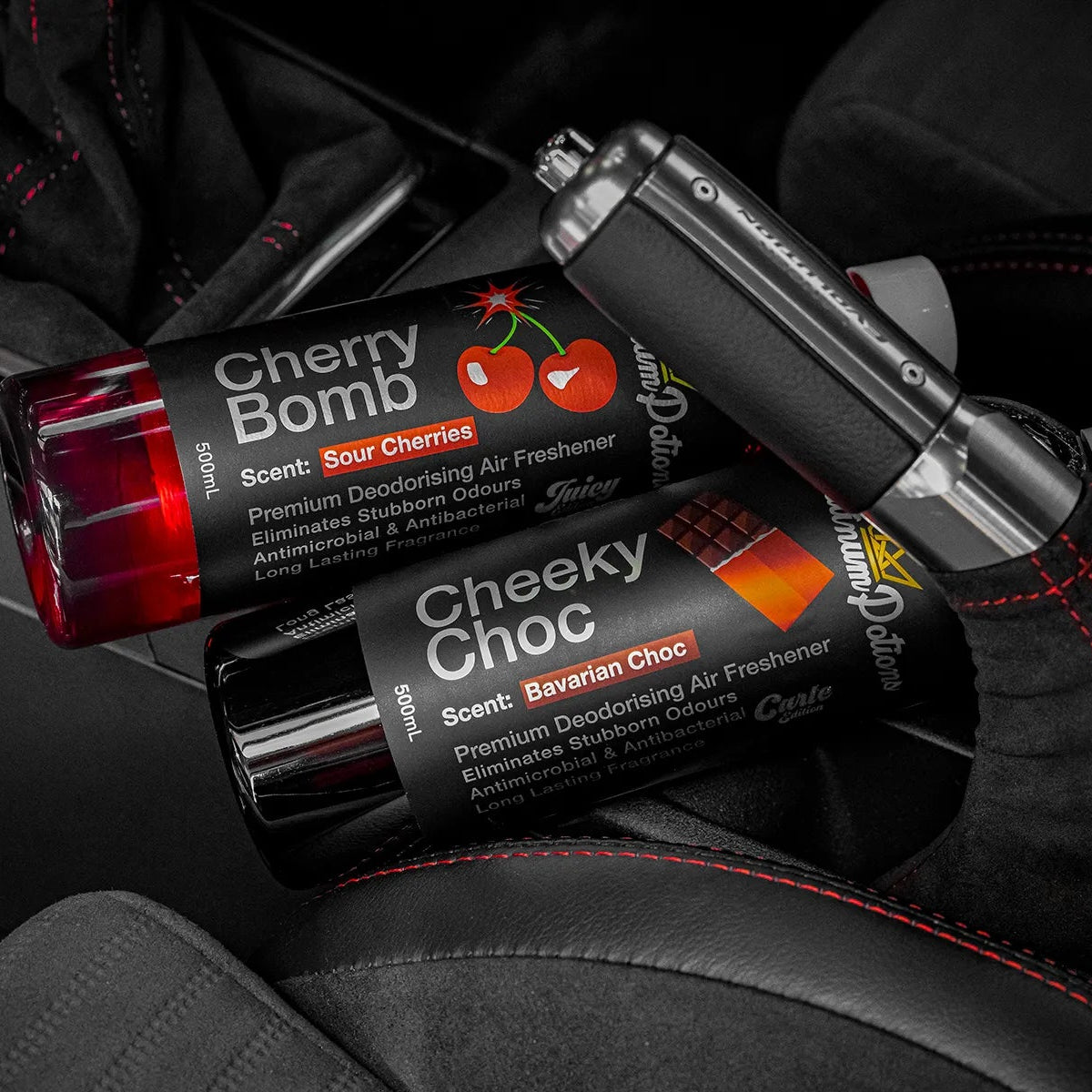 Two air freshener sticks, 'Cherry Bomb' and 'Cheeky Choc', on a car seat.