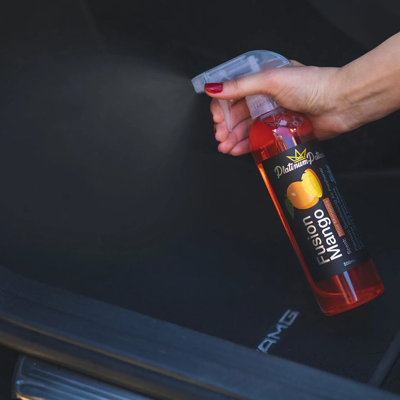 Person holding a bottle of 'Fusion Mango' spray air freshener inside a car.