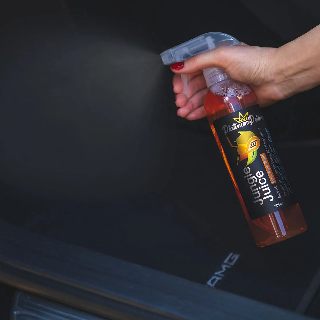 Person holding a bottle of car air freshener spray over a car seat