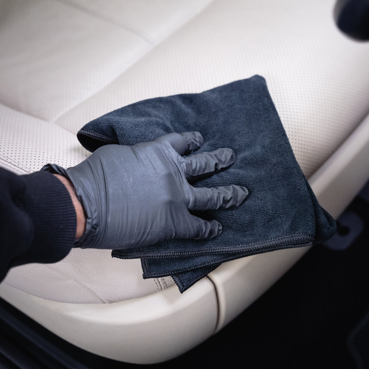 Person cleaning a car&#39;s steering wheel with a microfiber cloth and glove.