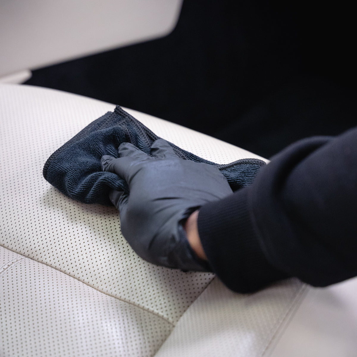 Person cleaning a car seat with a black cloth and glove