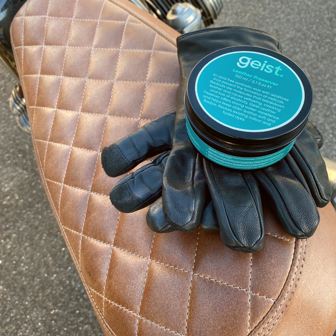 Pair of black gloves and a container labeled 'geist' on a quilted brown leather surface.