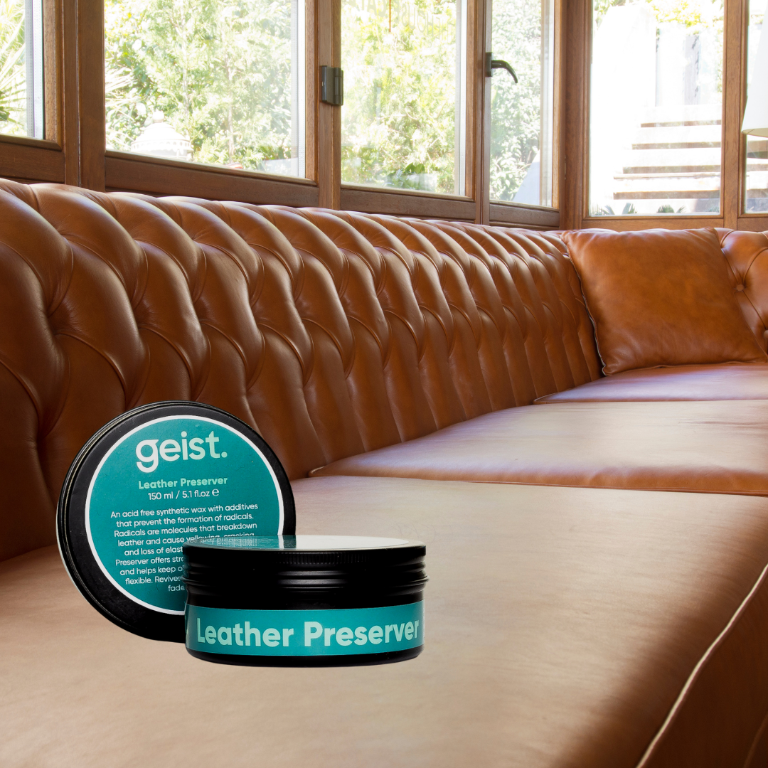 Geist Leather Preserver containers on a brown leather sofa with large windows in the background.