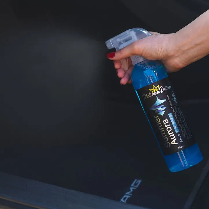 Person using a blue spray bottle labeled 'AquaLyn' on a car's black interior.