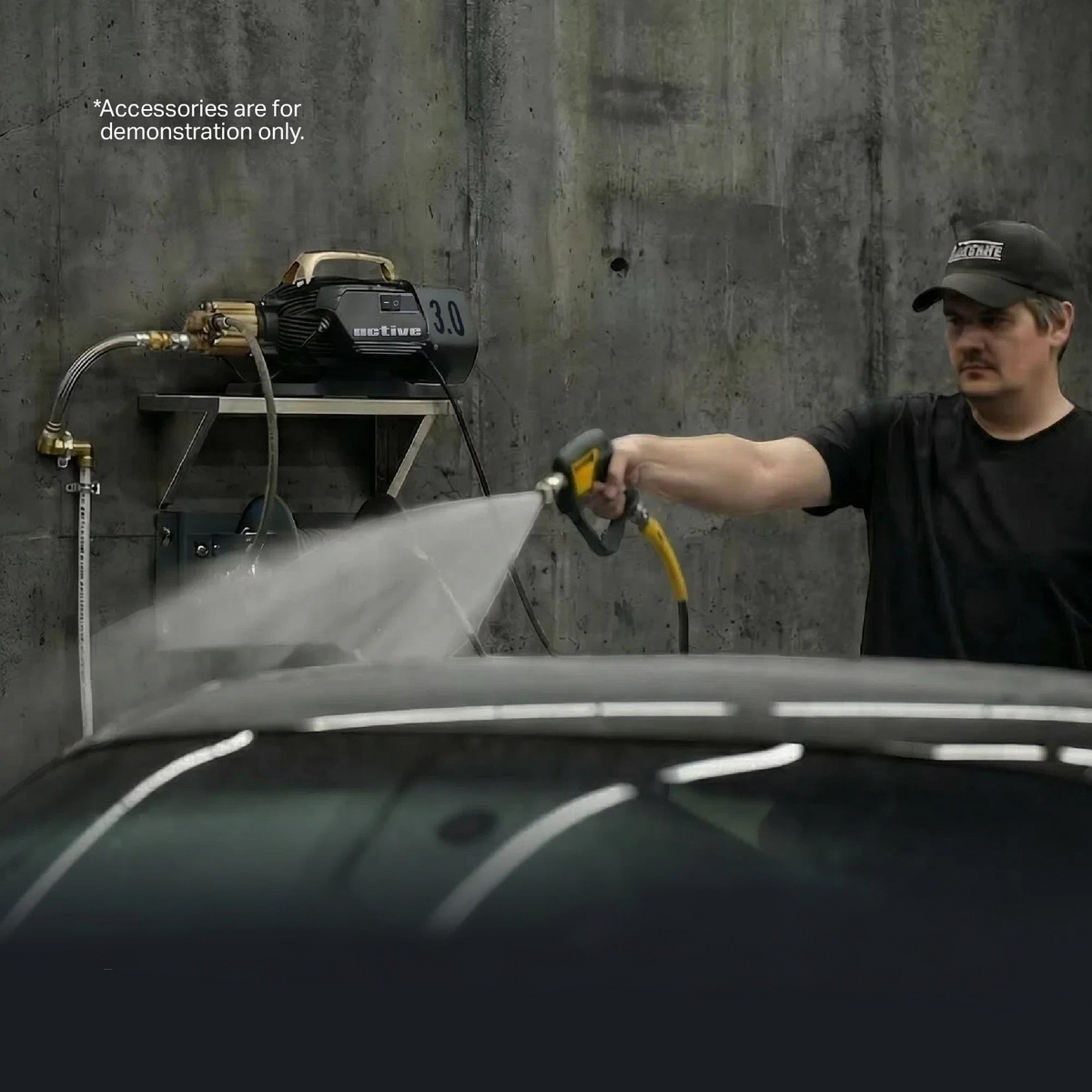 The Detail Warehouse Active 3.0 pressure washer mounted on a wall, being used by a man to spray water onto a car.