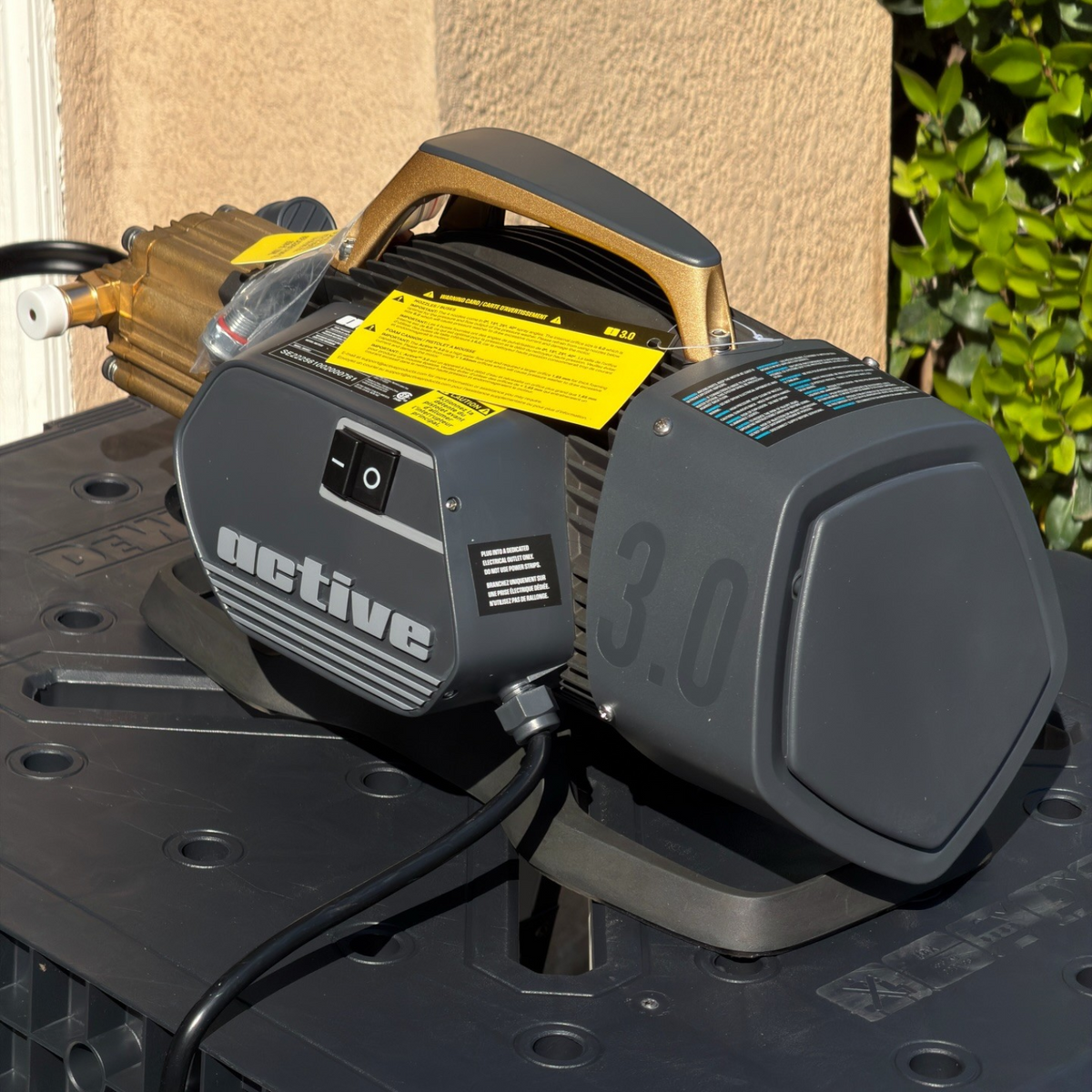 The Detail Warehouse Active 3.0 pressure washer featuring a grey housing, brass pump, and gold handle on a black table.
