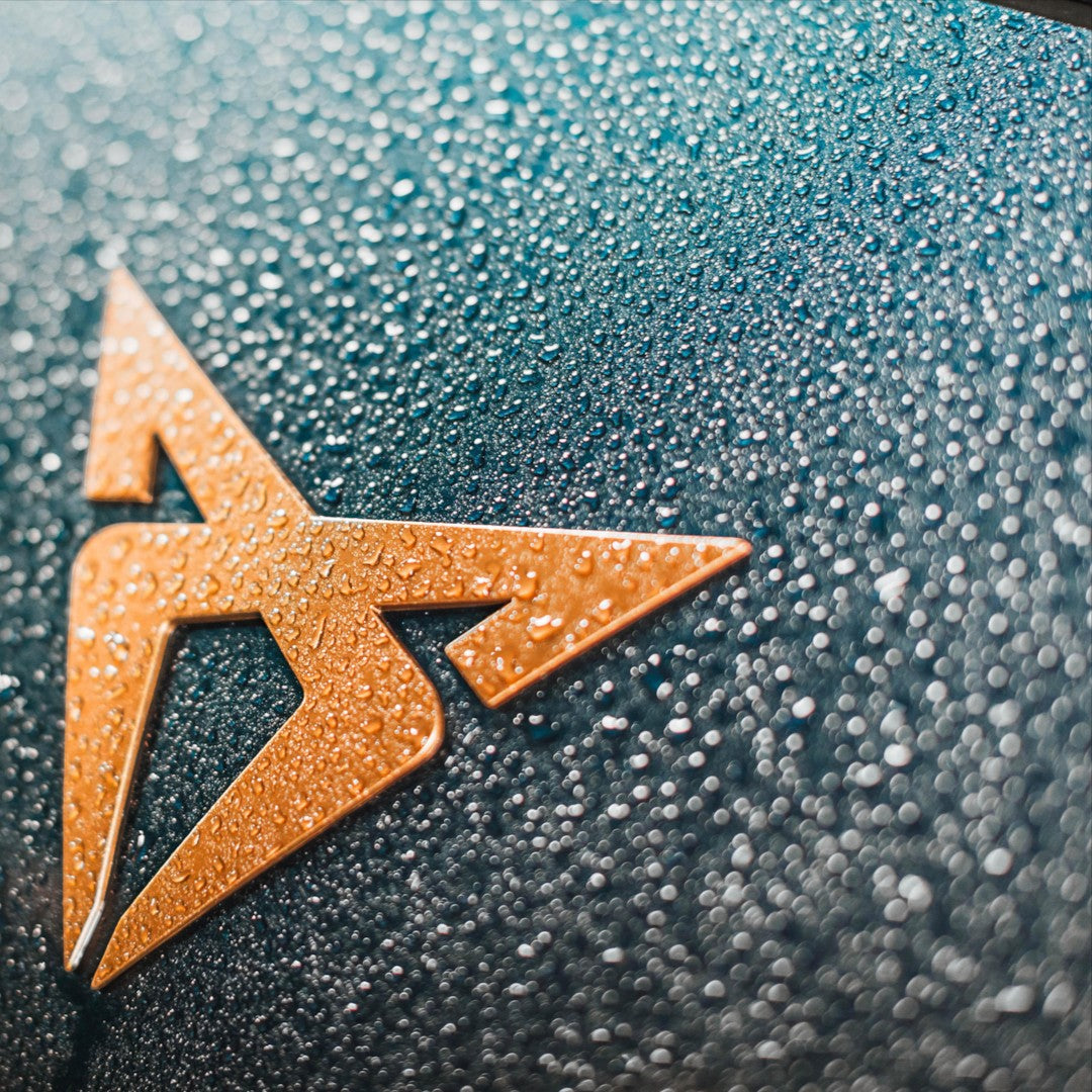 The Detail Warehouse Autoglym Aqua Wax applied to a car emblem showing hydrophobic water beading on dark paint