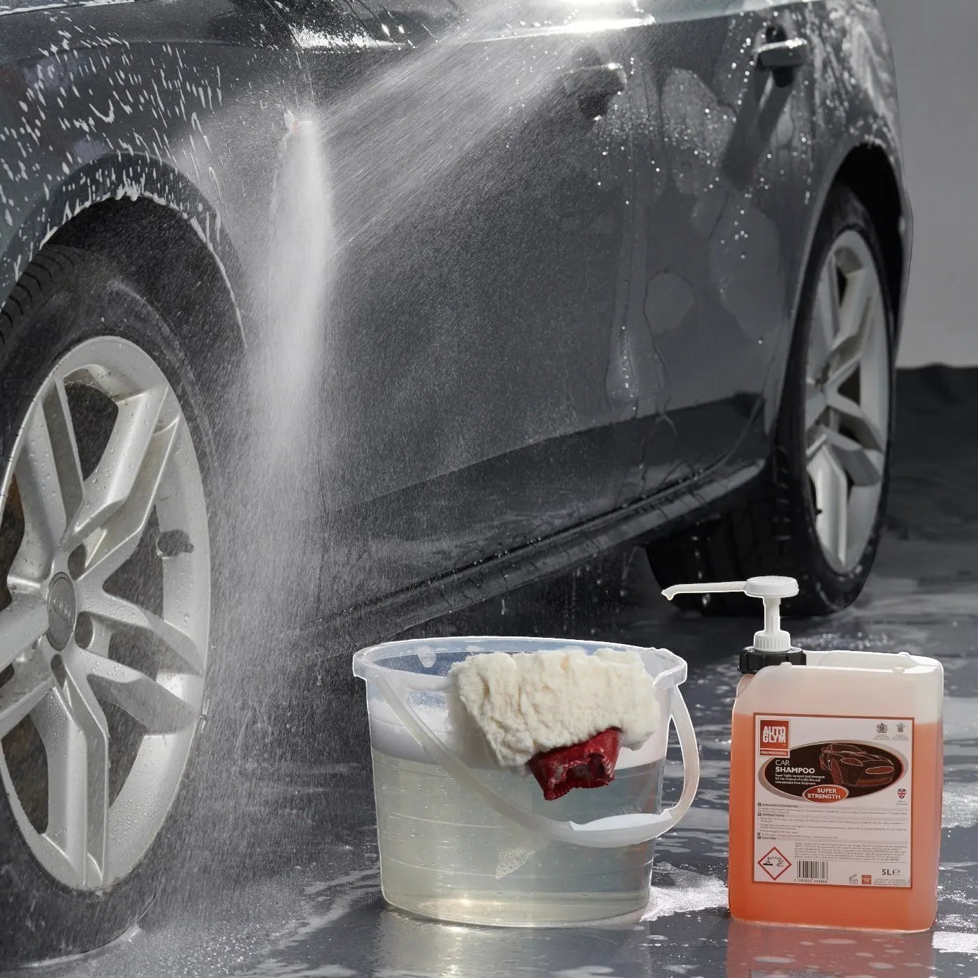 The Detail Warehouse Autoglym 5 litre car shampoo drum with dosing pump next to a bucket of soapy water and a car