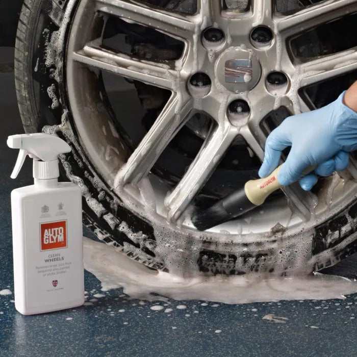 The Detail Warehouse Autoglym Clean Wheels spray bottle next to a car wheel being cleaned with a brush and foam