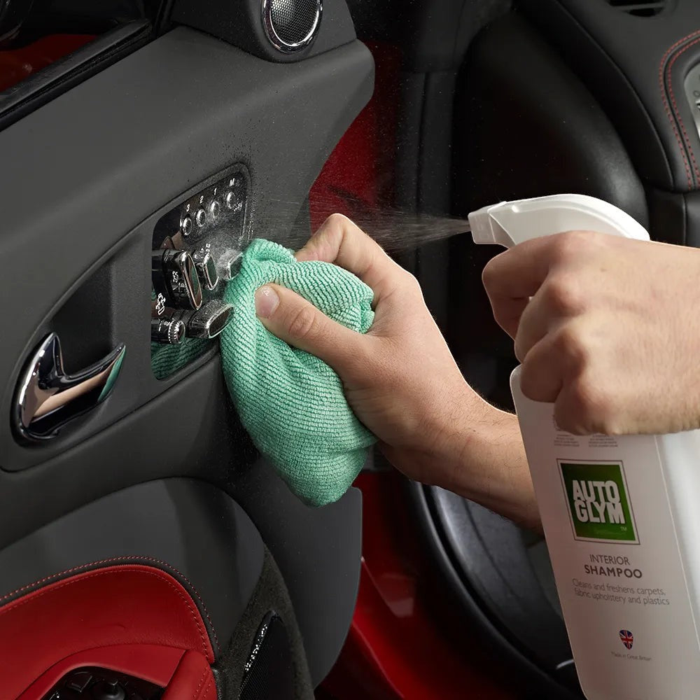 The Detail Warehouse Autoglym Interior Shampoo being sprayed onto a car door panel and wiped with a green cloth