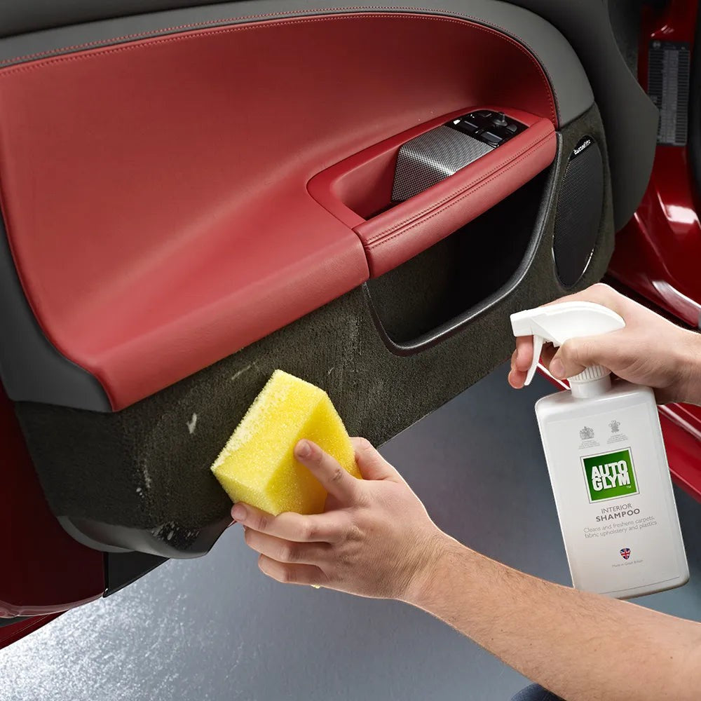 The Detail Warehouse Autoglym Interior Shampoo being used with a yellow sponge to clean a car door fabric panel