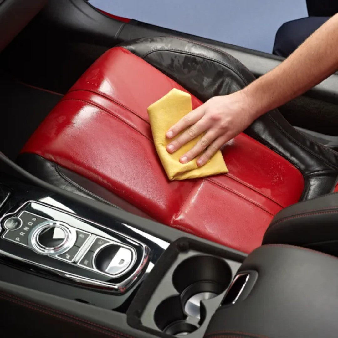 The Detail Warehouse hand using a yellow cloth to apply Autoglym Leather Cleaner to a red and black car seat