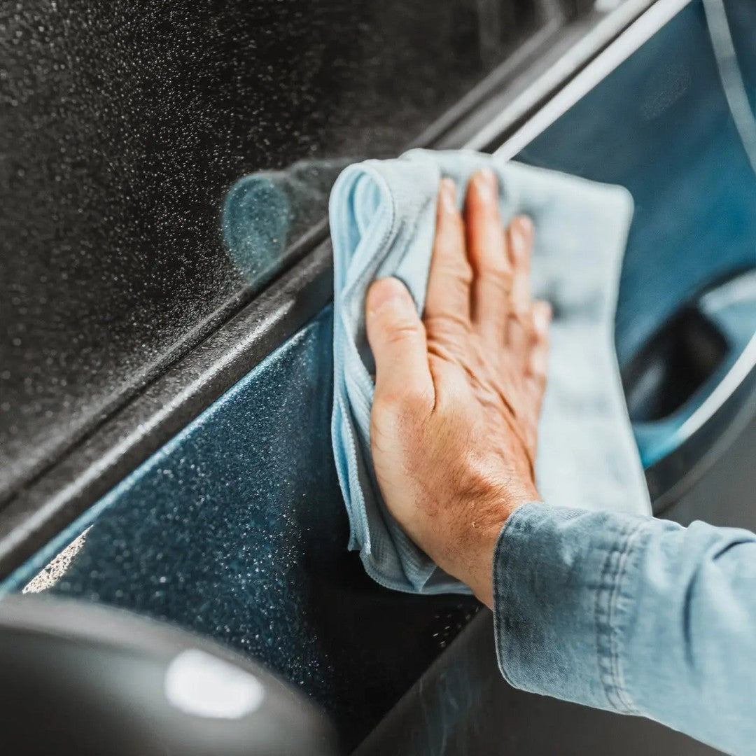 The Detail Warehouse hand buffing a wet dark blue car door with a light blue microfiber cloth after applying wax