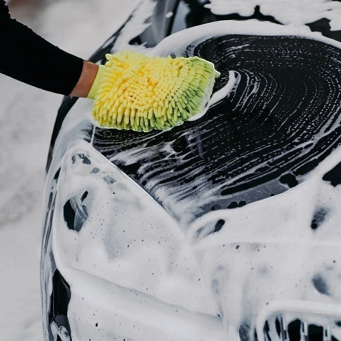 The Detail Warehouse branded yellow and green wash mitt cleaning a black car covered in thick white shampoo foam