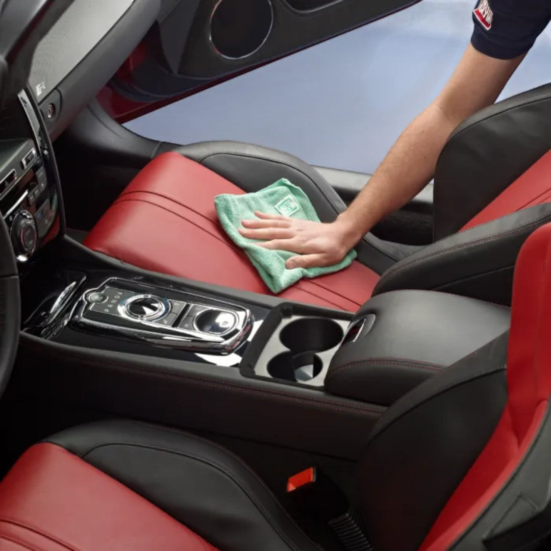The Detail Warehouse professional cleaning red and black leather car seat with a green microfibre cloth