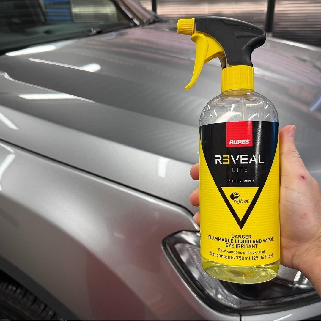 The Detail Warehouse Rupes Reveal Lite residue remover spray bottle held in front of a silver car hood.