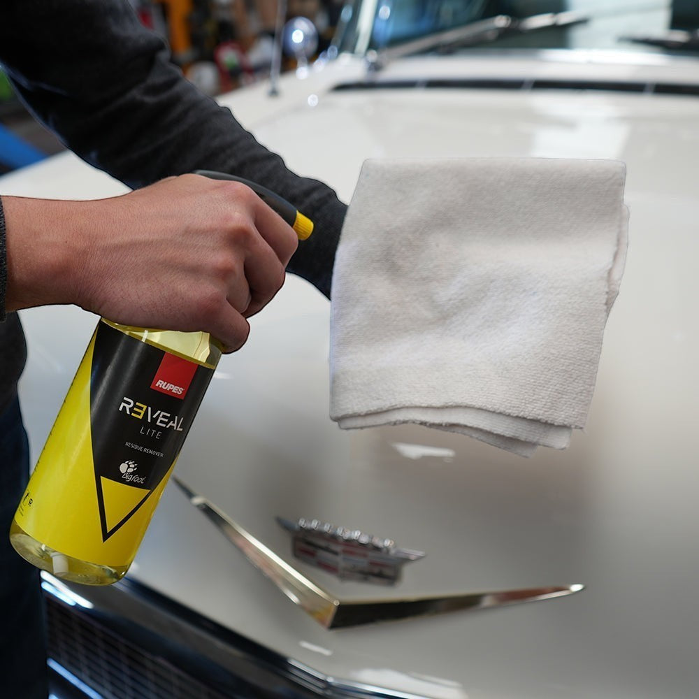 The Detail Warehouse user spraying Rupes Reveal Lite residue remover onto a white car hood with a microfiber cloth
