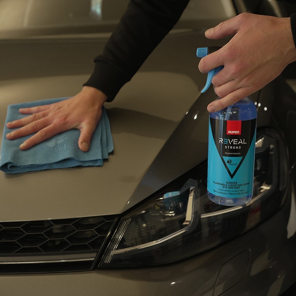 The Detail Warehouse Rupes Reveal Strong residue remover spray bottle being used to clean a car hood with a cloth.