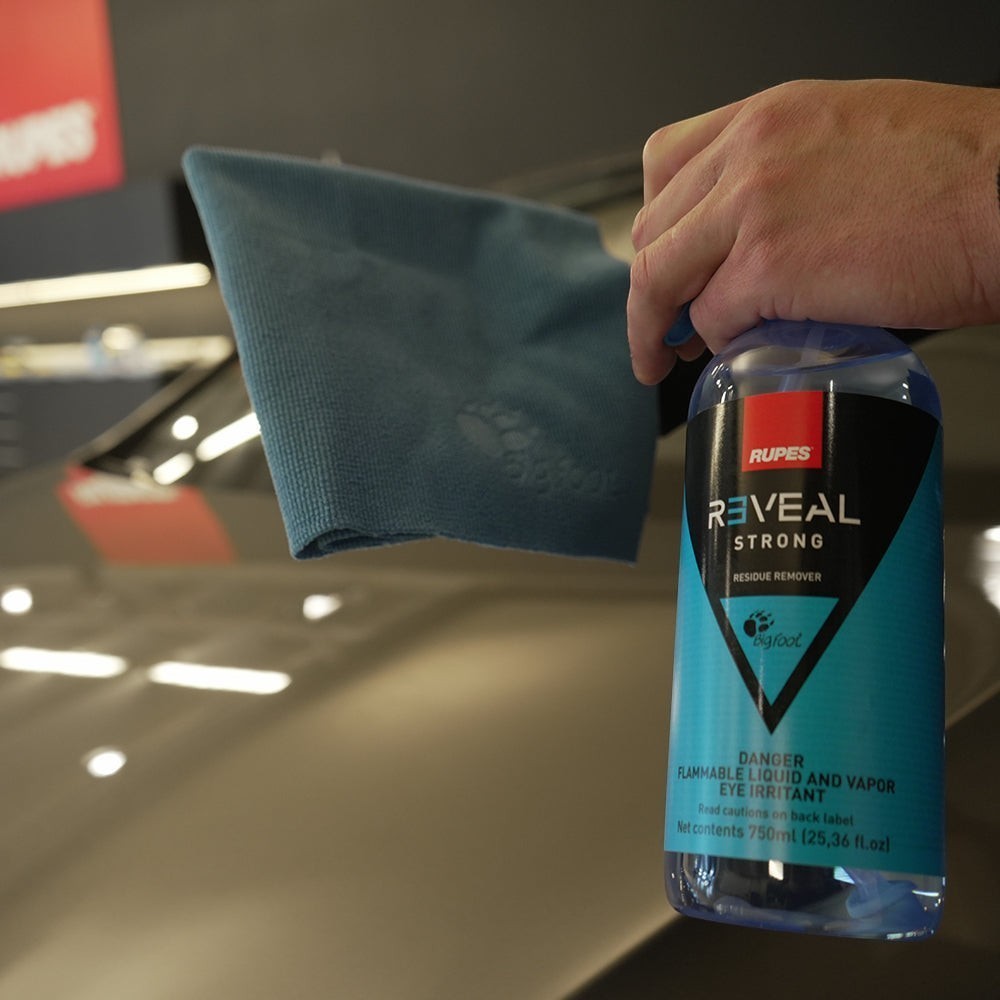 The Detail Warehouse hand holding a bottle of Rupes Reveal Strong residue remover and a blue microfiber cloth
