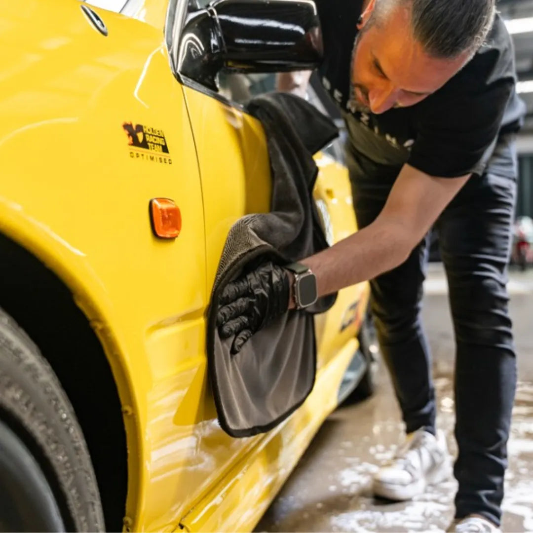 Person washing a yellow car with a black glove