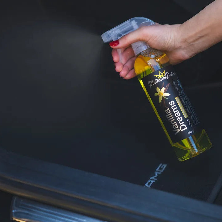 Person holding a bottle of car air freshener in front of a car's open door.